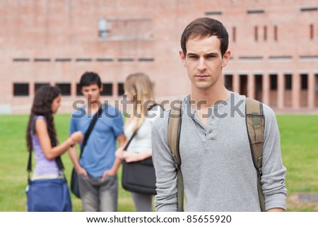 Lonely male student posing while his classmates are talking outside a building
