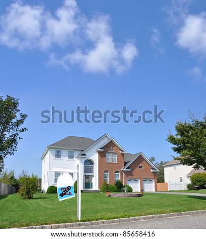 For Sale Real Estate Sign on Front Yard Lawn of Large Brick and Siding Luxury Two Car Garage Suburban Residential District Neighborhood Home on Beautiful Sunny Blue Sky Day