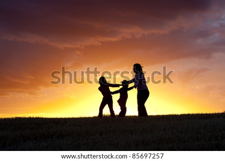 A mother and her two kids play ring around the rosie at sunset. Royalty-Free Stock Photo #85697257