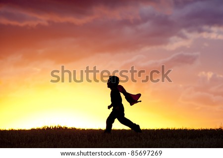 A young boy wearing a cape plays a super hero at sunset. Royalty-Free Stock Photo #85697269