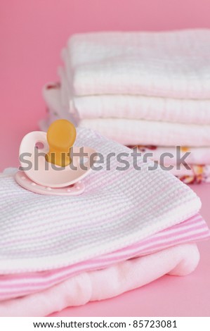 Pacifier and a pile of pink baby clothes with cotton diapers in the background