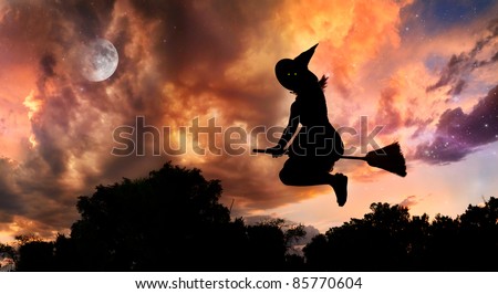 Halloween witch silhouette with glowing eyes flying on broomstick in the evening at dramatic sky with moon and stars