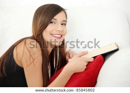 Beautiful woman reading a book, lying on a sofa in a living-room