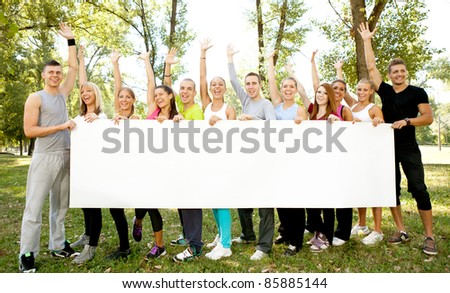 large group of people holding big white paper for advertisements, they are standing in the nature with their arms up and looking at the camera
