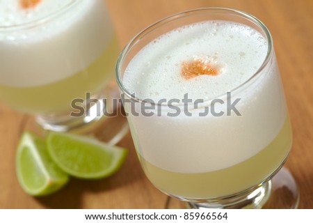 Peruvian cocktail named Pisco Sour made of Pisco (Peruvian grape schnaps),lime juice, syrup, egg white, and angostura (bitter fluid) drops on top (Selective Focus, Focus on the front of the angostura) Royalty-Free Stock Photo #85966564