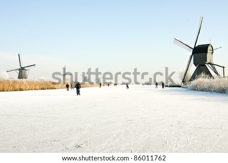Typically dutch: ice skating on a frozen lake at Kinderdijk with view on a windmill on a cold winterday