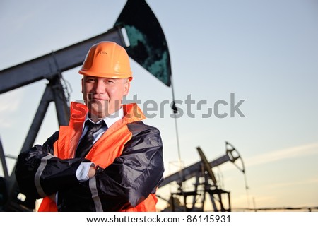 Oil worker in orange uniform and helmet on of background the pump jack and sunset sky.