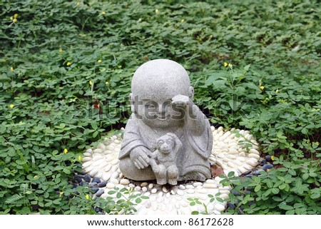 Granite statue of a cute baby monk playing with a monkey in a green park. Monkey is the ninth animal zodiac sign in the Chinese horoscope.