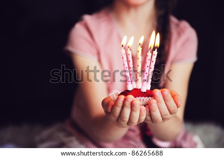 Close-up photo of a cupcake with five lighted candles in child's hands, focus on a cupcake