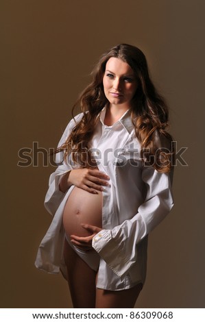 Picture of standing young pregnant woman in white top