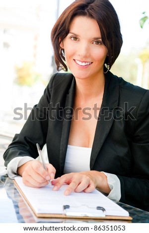 Closeup portrait of pretty woman sitting at cafe and signing documents while drinking her coffee. Natural light Outdoors