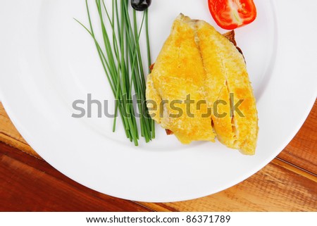 main portion: served roast golden fish fillet over white plate on wooden table with tomatoes and olives