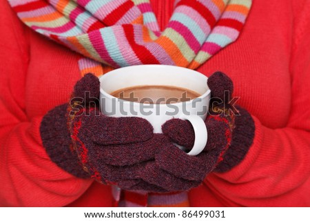Close up midriff photo of a woman wearing a red jumper, woolen gloves and a scarf holding a mug full of hot chocolate, good image to convey a feeling of winter and warmth.