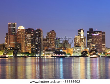 Boston downtown skyline panorama with skyscrapers over water with reflections at dusk illuminated with lights.