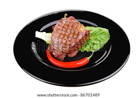 meat savory : beef grilled and garnished with green lettuce and red chili hot pepper on black dish isolated over white background