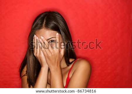 Playful shy woman hiding face laughing timid. Cute Chinese Asian / Caucasian woman smiling happy through hands. Red background. Royalty-Free Stock Photo #86734816