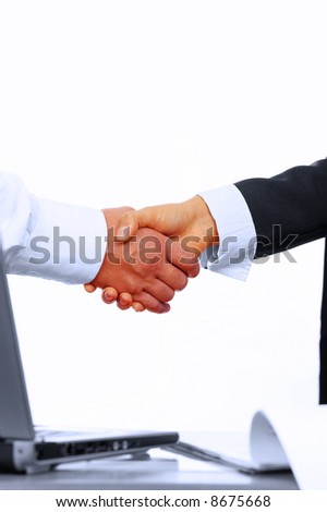 view of handshake over paper and computer in the background
