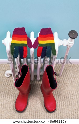 Photo of stripey gloves and red wellies drying on an old traditional cast iron radiator in a hallway, good image for winter related themes.