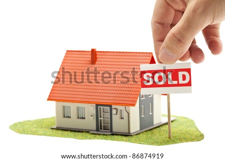 Hand holding "sold"-sign in front of model house - real estate buying concept