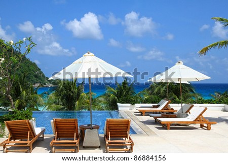 Sunbathing Beds with white umbrellas along the swimming pool by the sea, beautiful beach holiday scene