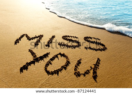 Dramatic inscription "Miss You" on wet golden beach sand in sunset light