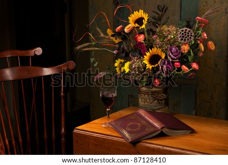 Floral still life with wine and gold embossed leather bound book, on an antique wooden table. Low key, dark background, spot lighting, and rich Old Masters colors. Horizontal format  and copy space.