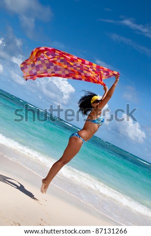 Tanned young europen women with red and orange pareo jump on white sand beach in summer