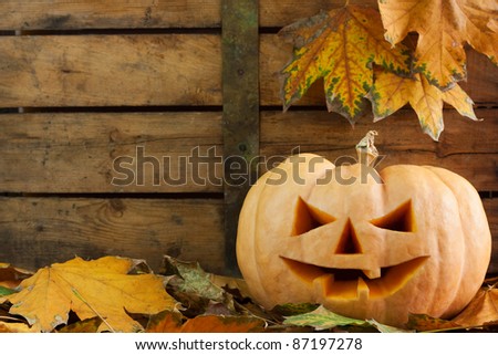 Creepy carved Halloween pumpkin face on wooden background and autumn leafs