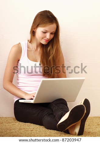 A young girl with a laptop sitting on the floor next to the wall
