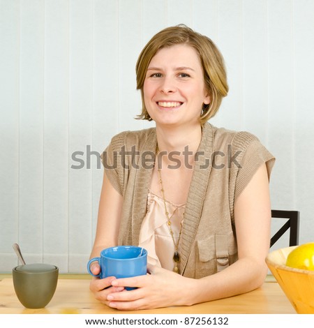 Portrait of relaxed woman holding a cup of coffee in her kitchen at her table