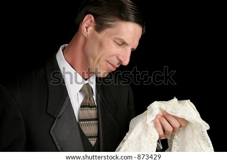 A grieving widower holding his wife's dress and smiling sadly as he remembers her.
