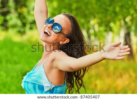 Portrait of beautiful dark-haired cheerful woman wearing blue top and sungrasses at summer green park.