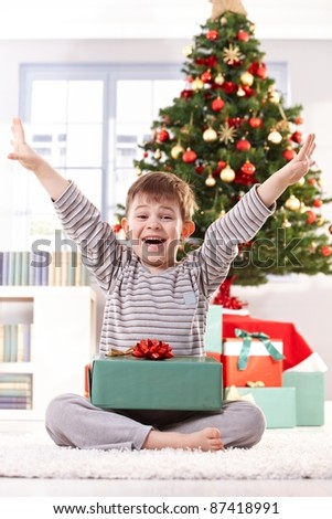 Happy little boy in pyjama getting present at christmas, laughing at camera with arms wide open.?