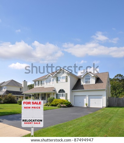 For Sale Real Estate Sign at Driveway Edge of Two Car Garage Suburban Home in Residential District Blue Sky with Clouds Day