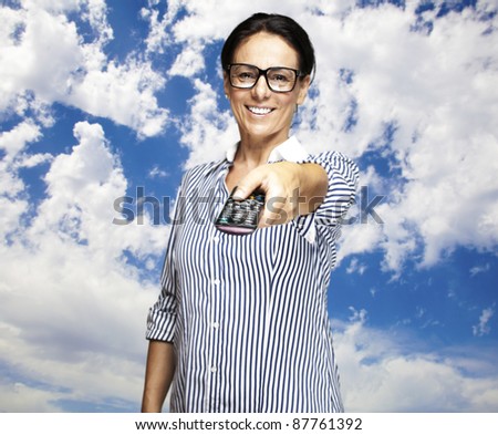 portrait of a middle aged woman using tv control against a cloudy sky