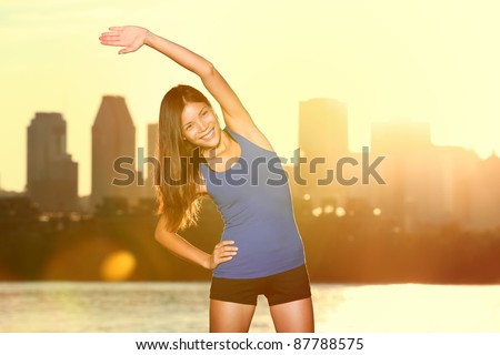 city runner stretching during exercising outdoors in city park with skyline in background. Beautiful young mixed race Asian / Caucasian fitness model training outside. From Montreal, Quebec, Canada.