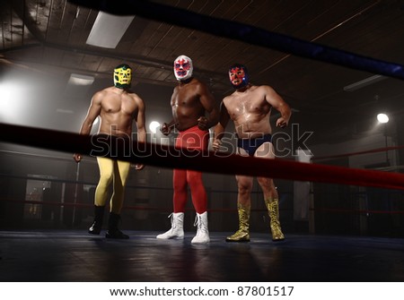 Three masked wrestlers stand in ring
