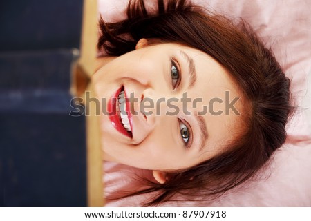 Closeup on reading teen girl`s smiling face lying on a pillow.