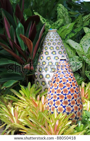 Big enameled vase with pretty flower patterns decorating the garden, surrounded by Bromeliad plant