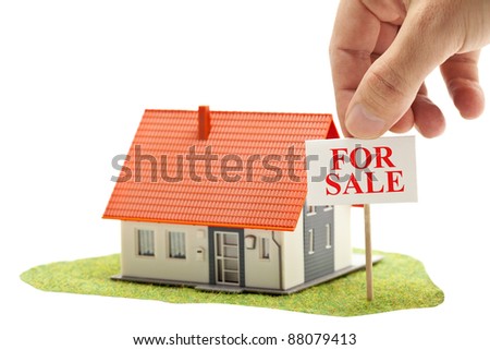 Hand holding "for sale"-sign in front of model house - real estate buying concept