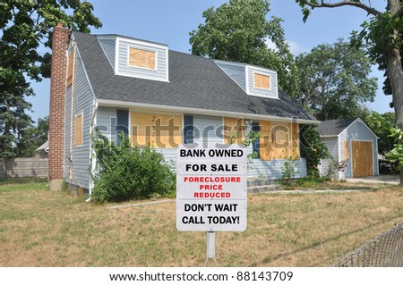 For Sale Bank Owned Real Estate Sign on Boarded Suburban Cape Cod Style Home in Residential Neighborhood