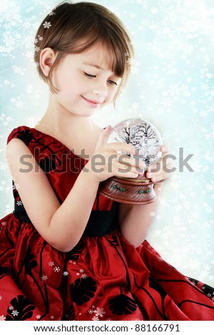 Happy little girl holding a Christmas snow globe. Shallow depth of field with selective focus on snowglobe in her hands.