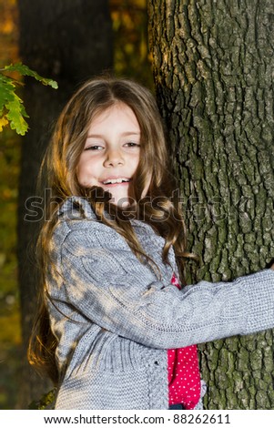 Happy little girl leaning on the tree