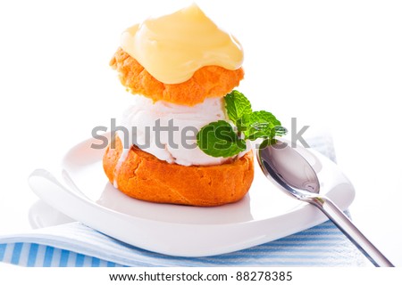 Profiterole in a small plate with ice cream vanilla sauce and mint leaf on a white backgound