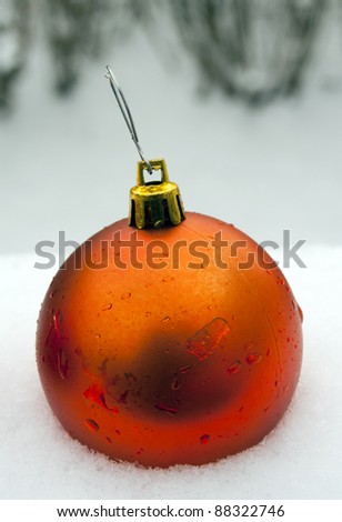 single orange christmas ornament in fresh snow with water droplets