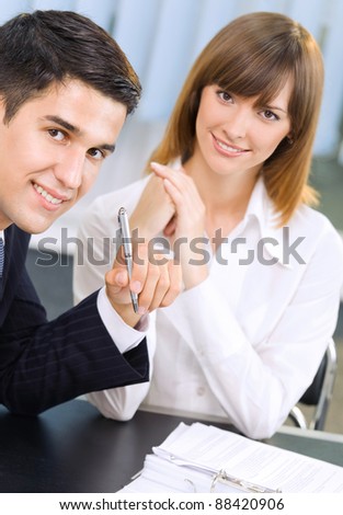 Two young happy smiling successful businesspeople working with document or contract at office