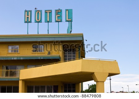 Vintage hotel sign with birds perched on top stands above a colorful motel on the side of the highway.
