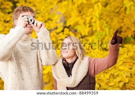 Young happy couple making photo in autumn park pointing at