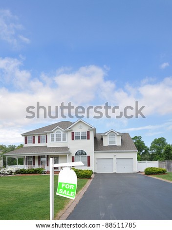 For Sale Sign on front yard of large two car garage suburban home in residential neighborhood on blue cloud sky day