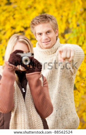Young happy couple woman making photo in autumn park pointing